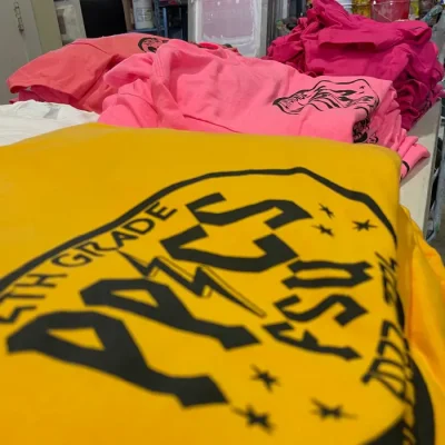 bulk-custom-printed-school-shirts-miami-epic-tees Stack of custom printed school event t-shirts in bright yellow and pink by Miami Epic Tees